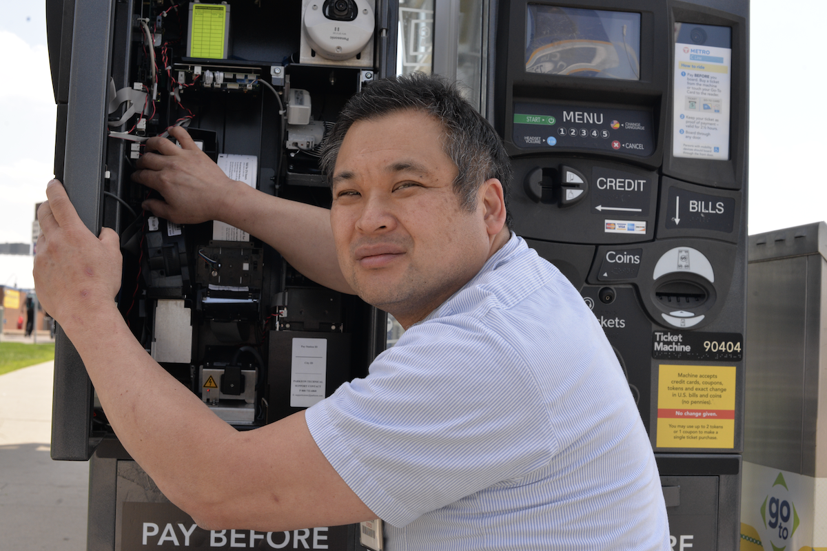 man kneeling working on open electronics of revenue equipment ticket vending machine