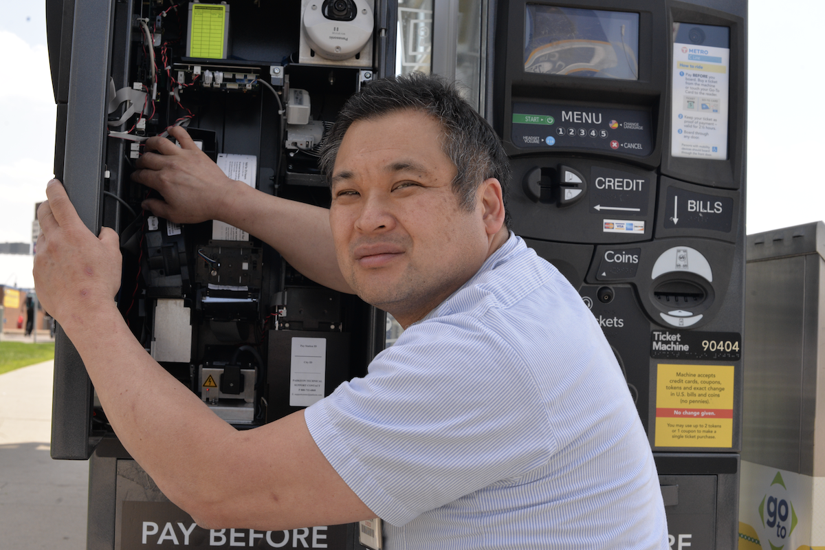 man kneeling working on open electronics of revenue equipment ticket machine