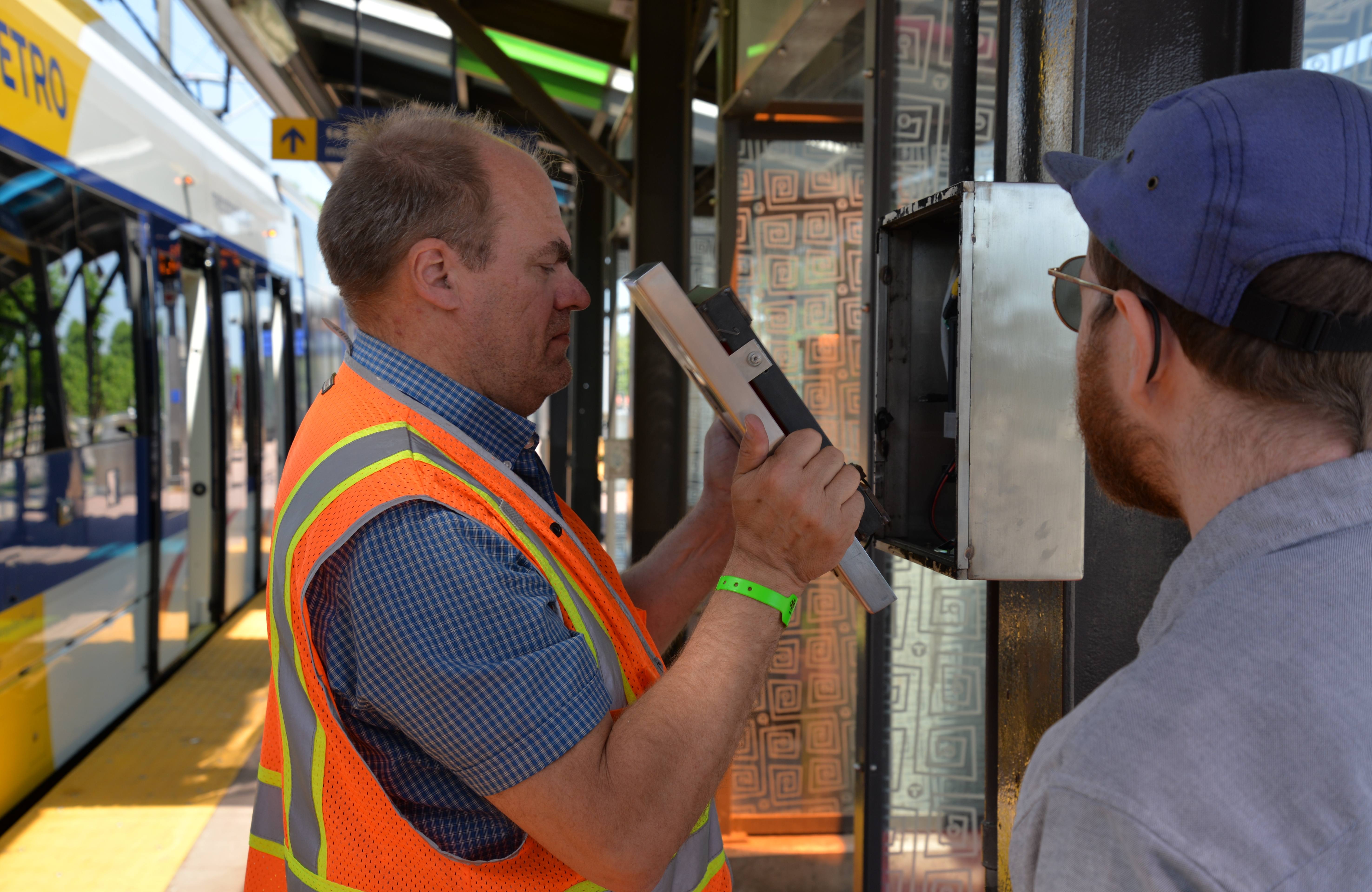 Public Art Administrator Mark Granlund and Max Hoaglund, an independent technologist, finish repairs to a box holding a video player at the METRO Blue Line’s 46th Street Station. 