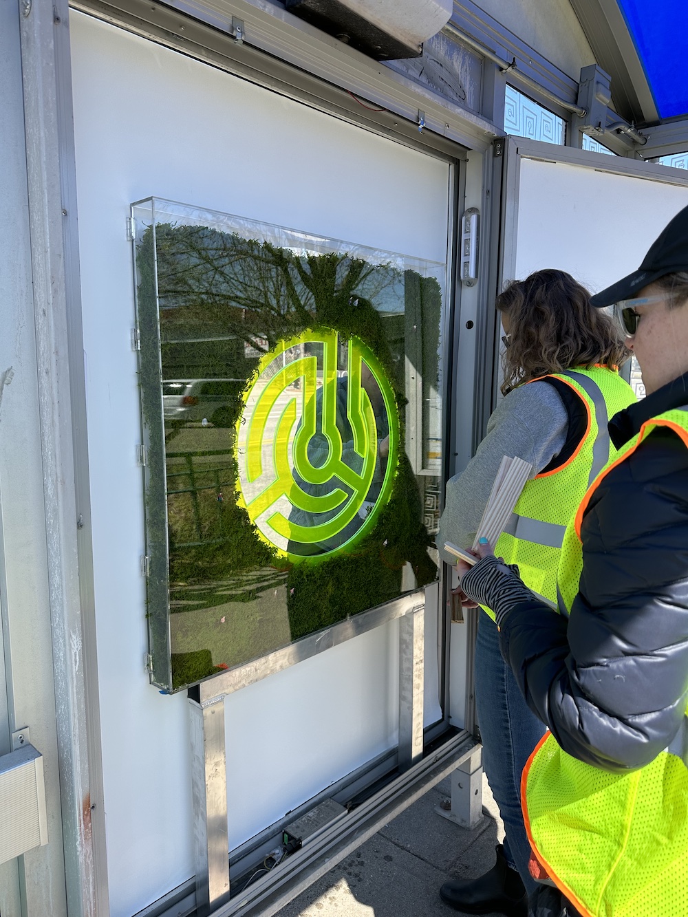 Two people installing artwork at a bus shelter.