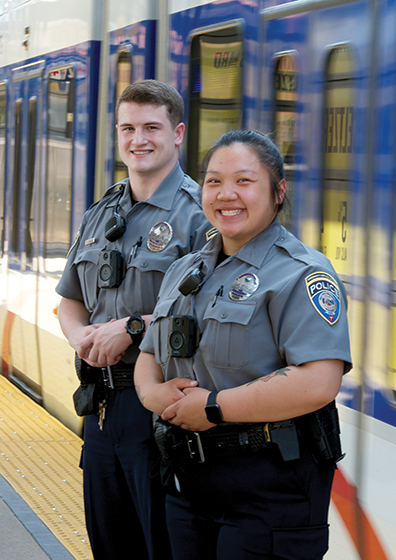 Two Community Service Officers stand next to a METRO light rail train