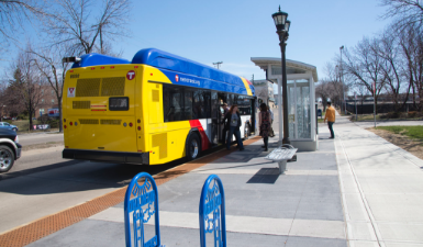 Blue and yellow bus with red trim at a but stop with passengers boarding.